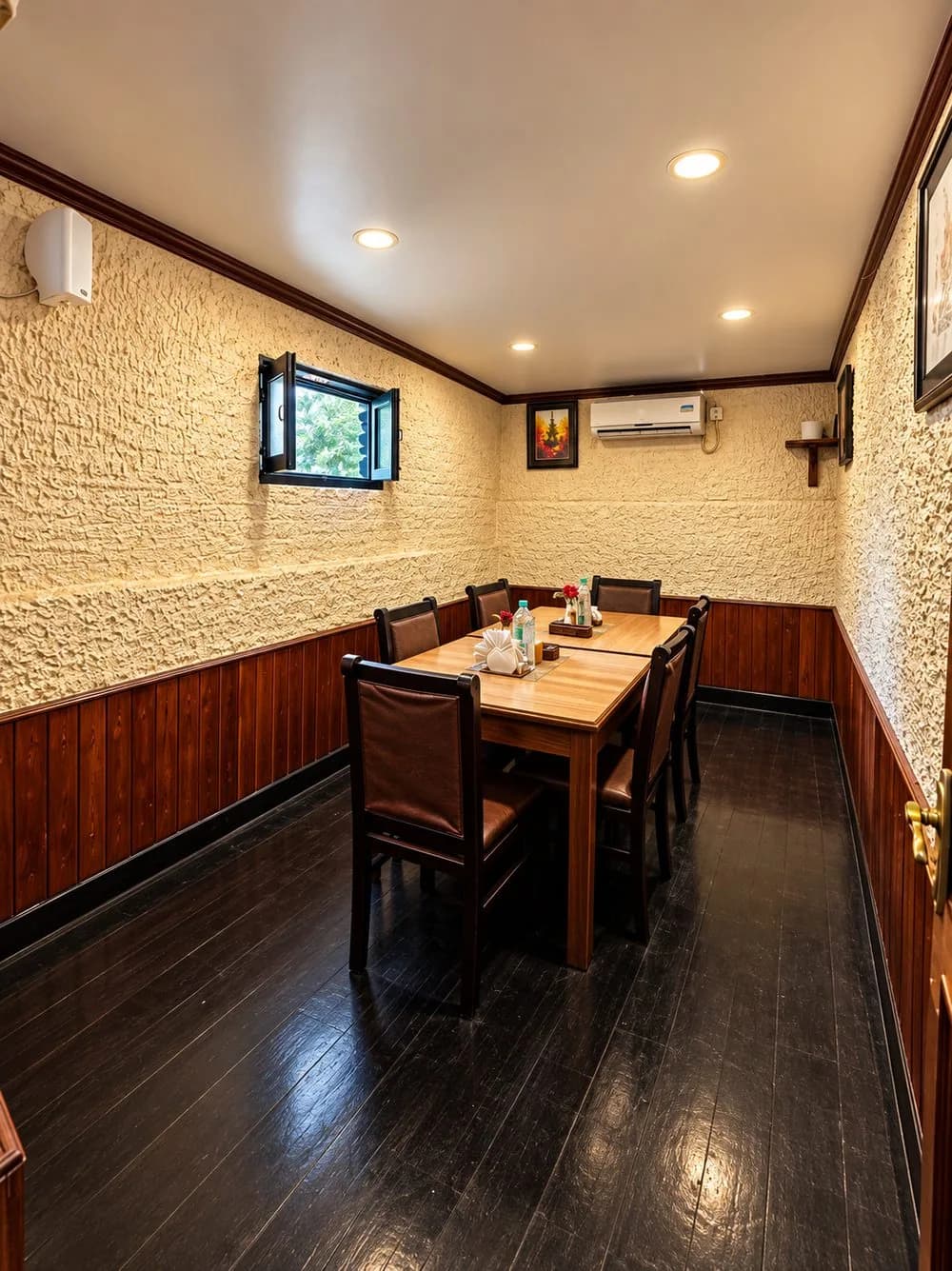 A private dining room seating six, with textured cream walls, wood panelling and a bright window.