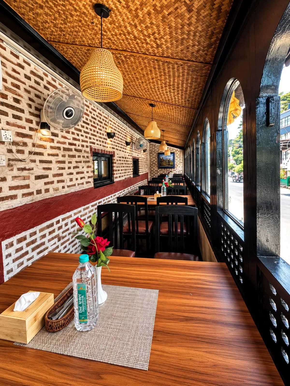 Street-side veranda with a brick wall, oxblood band, woven bamboo ceiling and rattan pendant lamps.